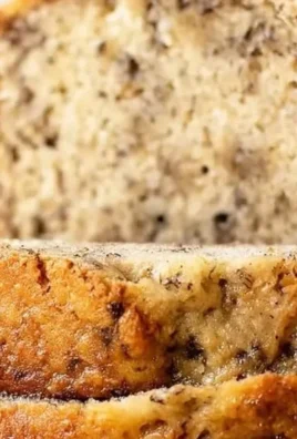 Freshly baked banana bread loaf with sliced bananas on a wooden table.