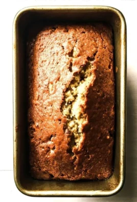 One banana banana bread with chocolate chips and walnuts on a wooden table.