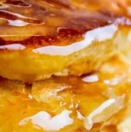 Fluffy pancakes stacked on a plate drizzled with syrup and topped with fruit.