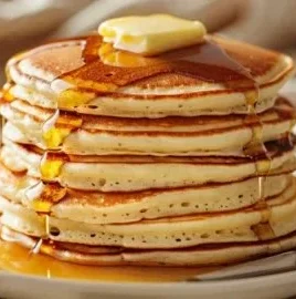 Fluffy pancakes stacked high on a plate, drizzled with syrup and berries