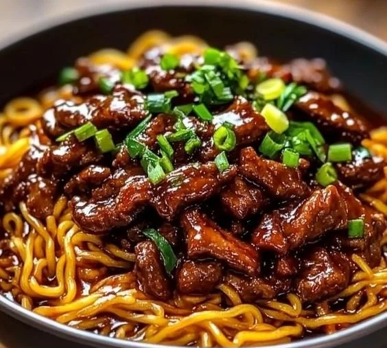Delicious sticky beef noodles served on a plate with vegetables.