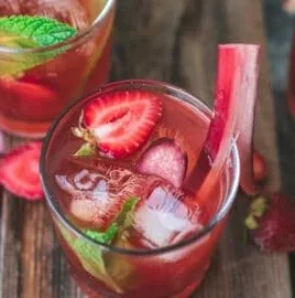 Bottle of Strawberry Rhubarb Fermented Soda in a glass on a wooden table.