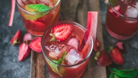 Bottle of Strawberry Rhubarb Fermented Soda in a glass on a wooden table.