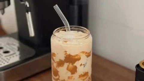 Delicious iced coffee served in a glass with ice and coffee beans