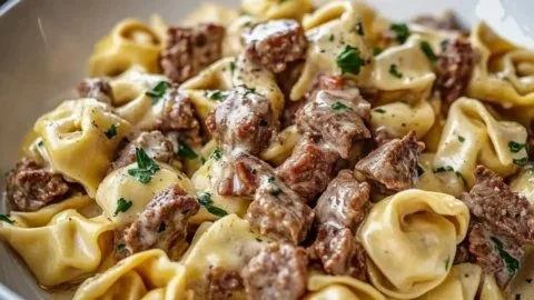 Delicious plate of Philly Cheesesteak Tortellini pasta topped with cheese and herbs.